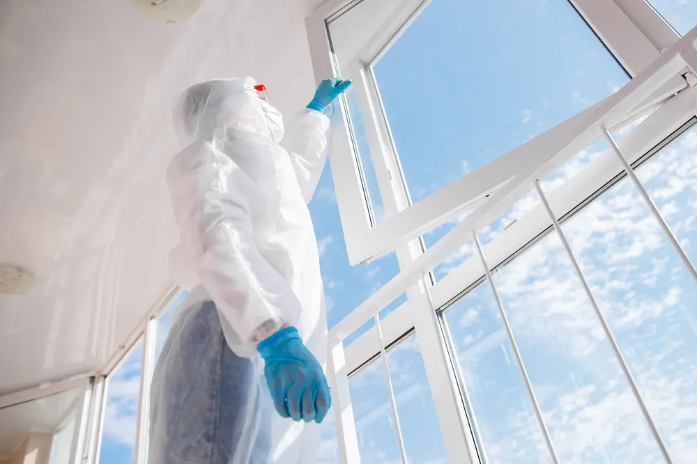 Technician in protective suit performing commercial pest control inside building.