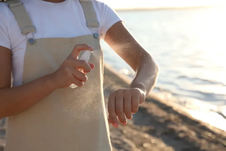 Person applying mosquito repellent spray to their arm to help prevent mosquito bites outdoors.