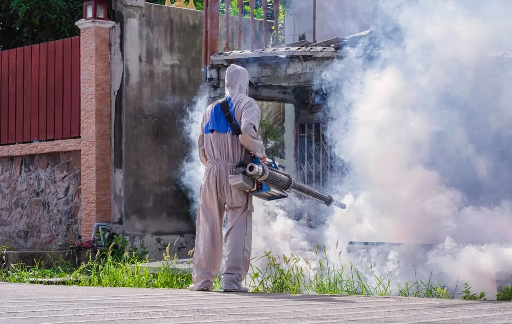 Pest control technician performing mosquito control fogging around a residential property.